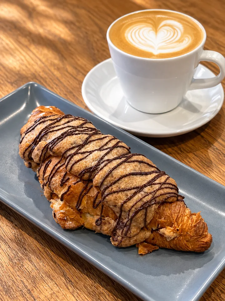 Latte art beside a chocolate croissant